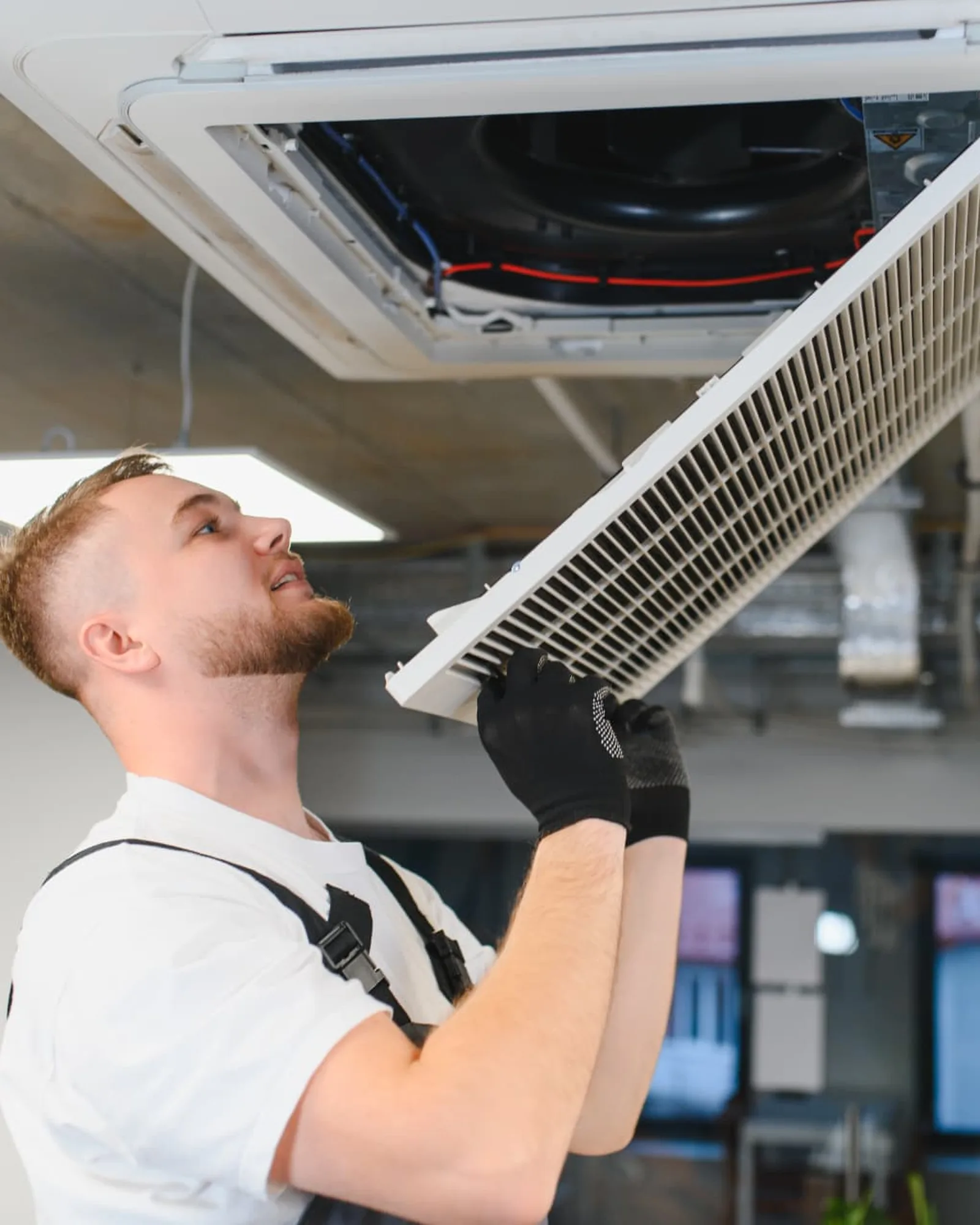 Tekniker der servicerer et ventilationsanlæg i loftet på en arbejdsplads